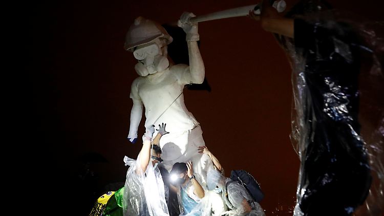 "Lady Liberty" thront mit Regenschirm, Atemmaske und Helm bewaffnet auf einem Gipfel bei Hongkong.