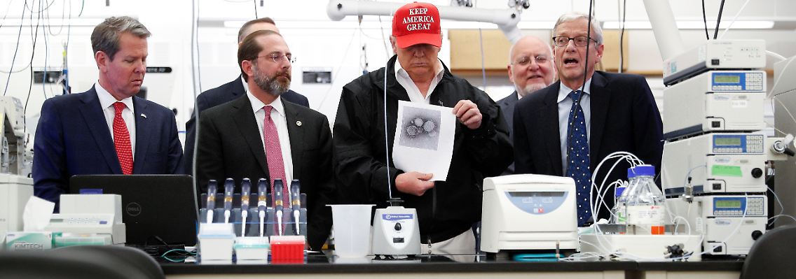 Ortstermin in der US-Seuchenkontrollzentrale CDC: US-Präsident Donald Trump trägt Wahlkampfkappe und zeigt ein ausgedrucktes Coronavirus-Bild vor.