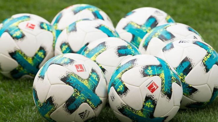 Fußbälle liegen vor dem Spiel auf dem Rasen. 