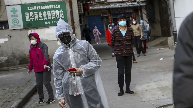 Ein Mann liest auf seinem Smartphone, während er in Wuhan für Fleisch ansteht.