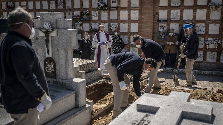Mit Mundschutz begleitet ein Priester auf einem Friedhof in Madrid die Beerdigung eines Corona-Toten.