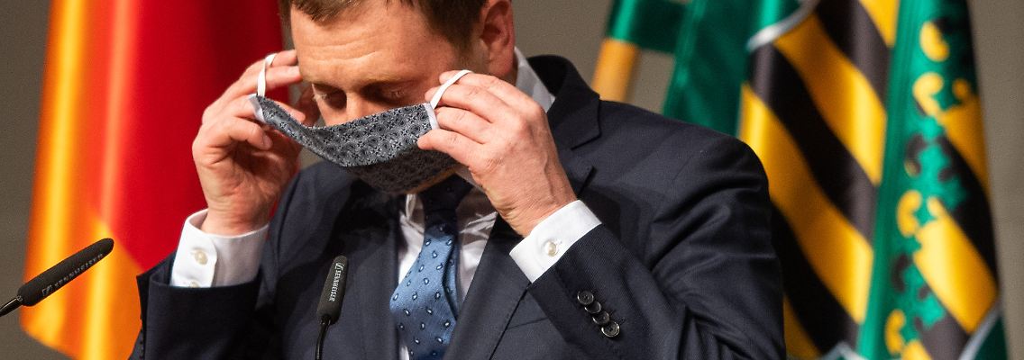 Kretschmer macht es schon einmal vor und präsentiert einen Mund-Nase-Schutz.