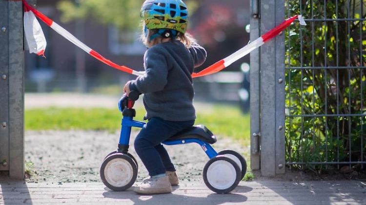 Ein kleines Mädchen steht vor einem abgesperrten Spielplatz.