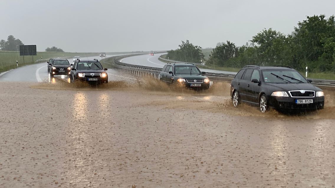 Autos fahren bei starkem Regen auf der zum Teil unter Wasser stehenden Autobahn 6 in Bayern.