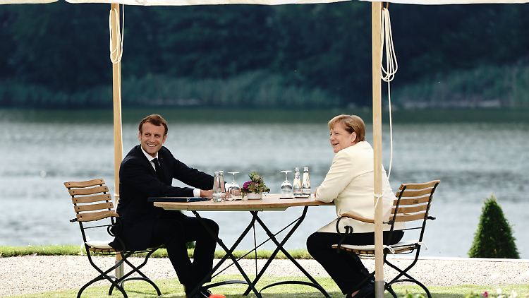 Nach langer Zeit wieder vereint: Emmanuel Macron und Angela Merkel sitzen im Park am Huwenowsee vor Schloss Meseberg.