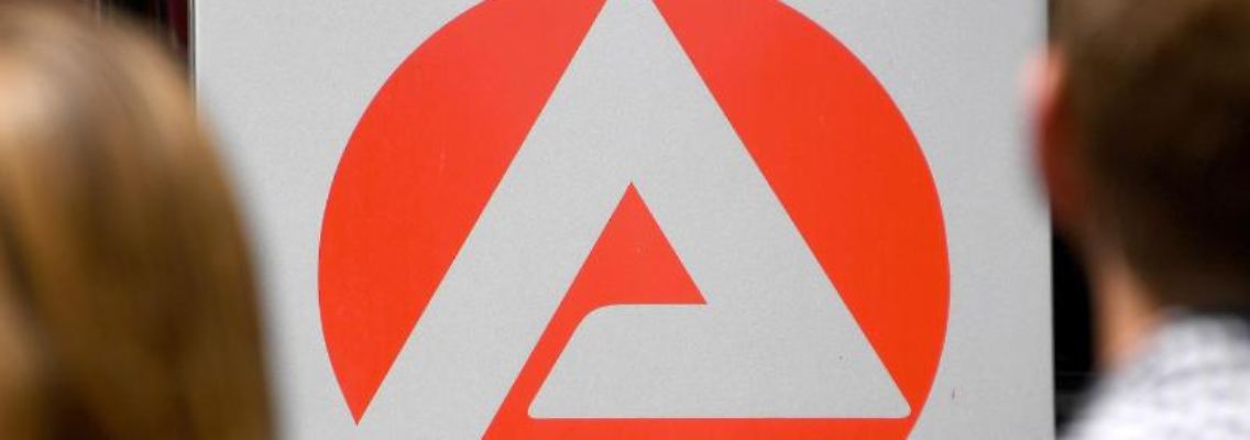 Zwei Personen stehen vor dem Logo der Agentur für Arbeit. Foto: Carsten Rehder/dpa