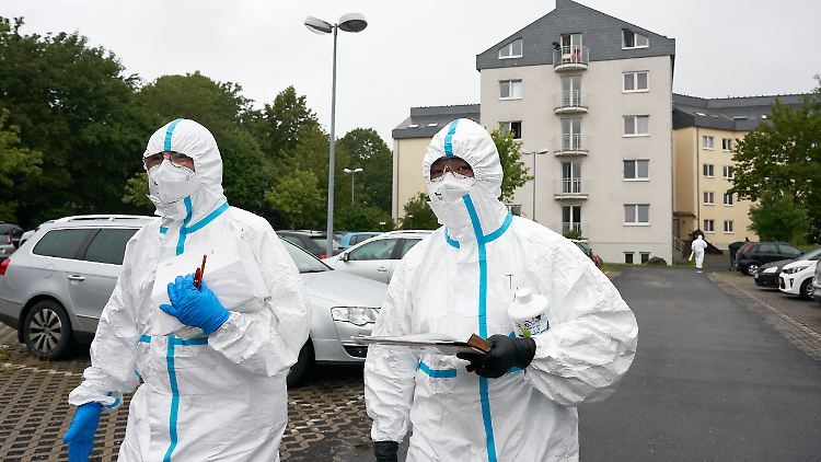 Einsatzkräfte in Schutzkleidung stehen vor einem der drei Studentenwohnheime.