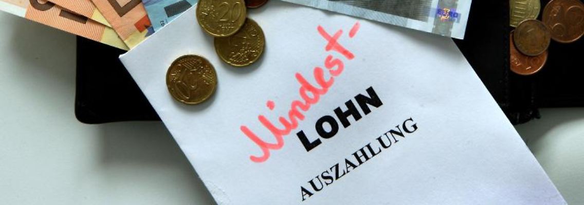 Geld liegt neben einem Zettel mit der Aufschrift "Mindestlohn". Foto: Jens Büttner/dpa-Zentralbild/dpa/Symbolbild