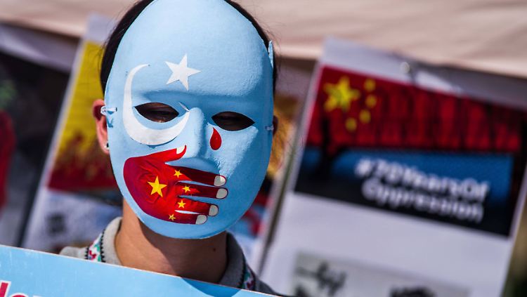 Ein Demonstrant trägt eine Maske mit den Farben der Flagge der uigurischen Unabhängigkeitsbewegung und einer aufgemalten roten Hand mit den Sternen der chinesischen Nationalflagge.