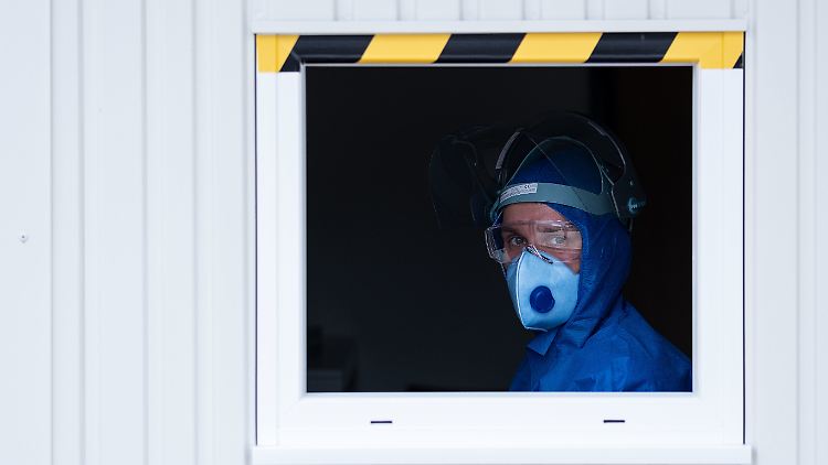 Ein medizinischer Mitarbeiter sitzt mit Vollschutz im Coronatest-Container auf dem Werksgelände der Volkswagen AG. 