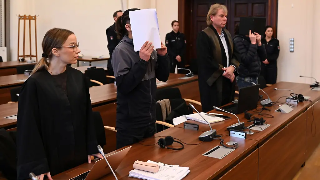 Die-Angeklagten-halten-sich-vor-Beginn-des-Prozesstages-Dokumente-vor-das-Gesicht