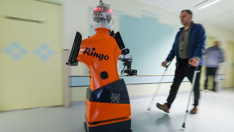 Ein Patient trainiert mit Hilfe von einem Roboter das Gehen auf einem Flur im Krankenhaus.