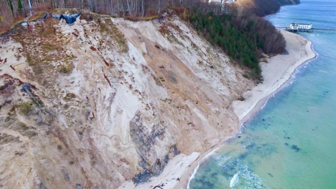 Der Sand eines abgerutschten Teils der Steilküste versperrt am Strand den Weg am Wasser entlang.