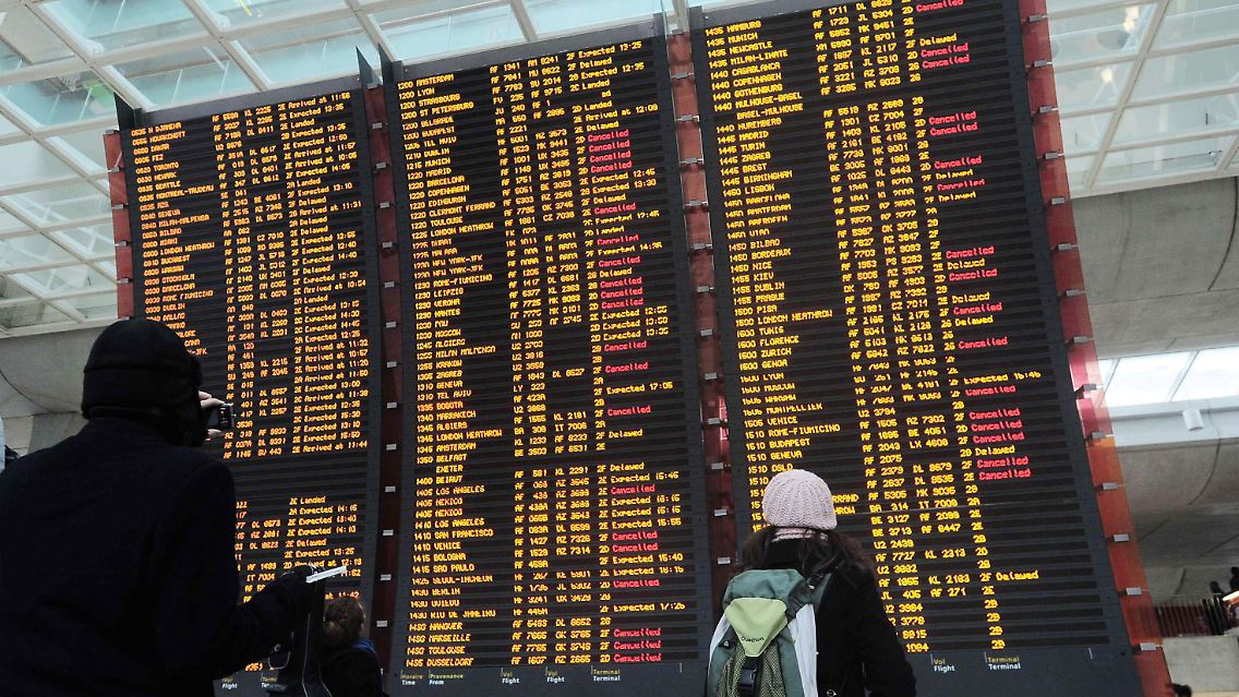 Verzweifelte Reisende betrachten die Flugtafel am Flughafen Charles de Gaulle.