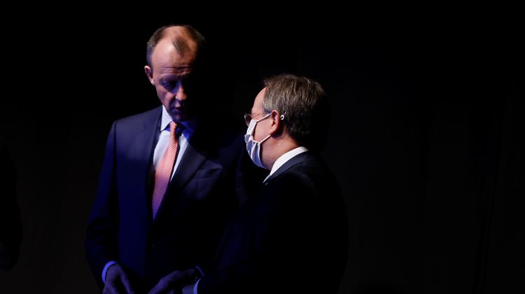 Merz und Laschet sprechen hinter der Bühne des Parteitags miteinander.