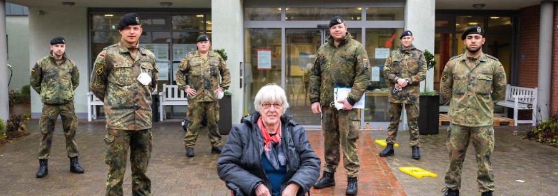 Bundeswehrsoldaten stehen vor einem Altenheim hinter einer Bewohnerin. Foto: Mohssen Assanimoghaddam/dpa