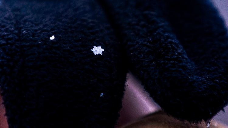 Schneeflocke auf einem Handschuh: Schneekristalle können unter dem Mikroskop wie Sterne oder Nadeln aussehen, aber sie haben immer eine hexagonale, also sechseckige Kristallstruktur.