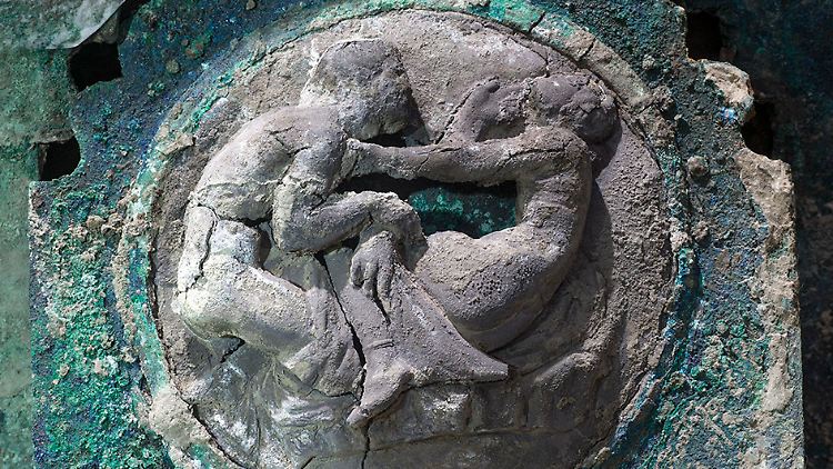 An der Seite ist der Wagen mit Dekorationen aus Zinn und Bronze verziert, die etwa Männer und Frauen in erotischen Szenen zeigen.