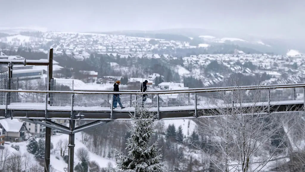 Spaziergaenger-gehen-eine-Bruecke-neben-der-Winterberger-Bobbahn-mit-Blick-auf-die-Landschaft-im-Schnee