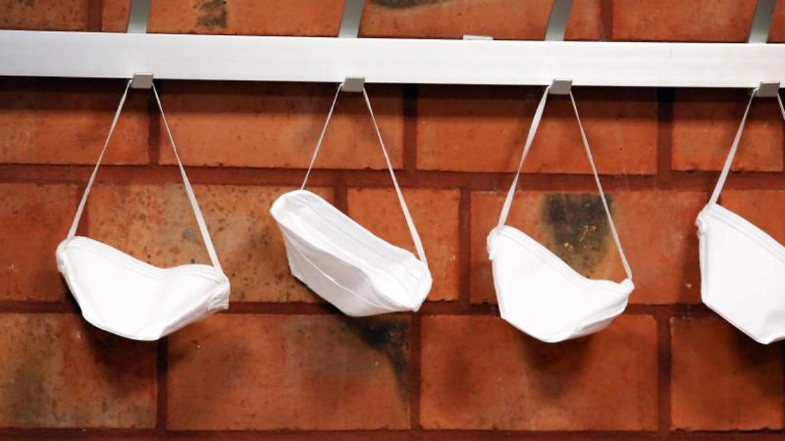 Mund-Nase-Schutzmasken hängen an Haken. Foto: Rene Traut/dpa/Symbolbild