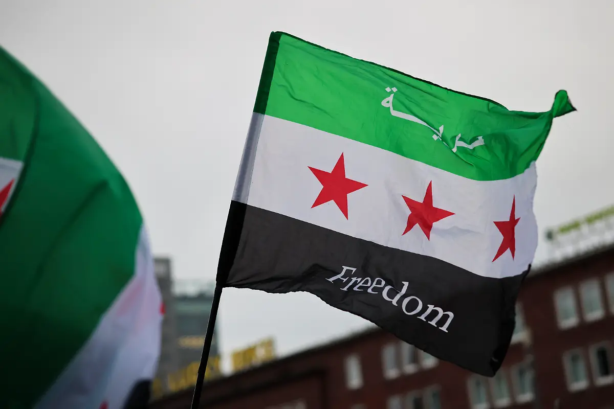 Die-Gegner-des-gestuerzten-Assad-Regimes-schwenken-mehrheitlich-eine-Flagge-mit-drei-horizontalen-Streifen-in-gruen-weiss-und-schwarz-In-der-Mitte-sind-drei-rote-Sterne-abgebildet