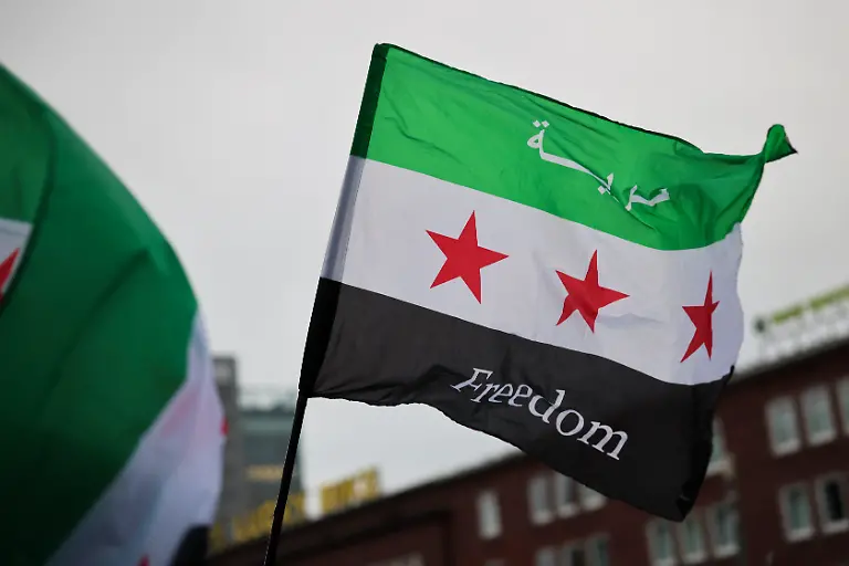 Die-Gegner-des-gestuerzten-Assad-Regimes-schwenken-mehrheitlich-eine-Flagge-mit-drei-horizontalen-Streifen-in-gruen-weiss-und-schwarz-In-der-Mitte-sind-drei-rote-Sterne-abgebildet