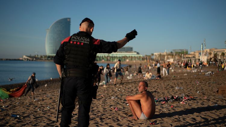 Ein Polizist fordert einen jungen Mann auf, den Strand bei Barcelona zu verlassen.