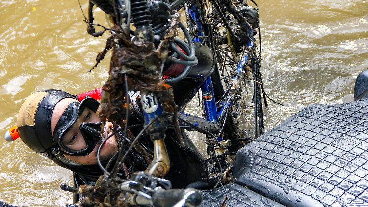 Hobbytaucher Noah Boonma hievt ein Fahrrad, das er in der Lahn gefunden hat, auf eine Plattform am Flussufer.