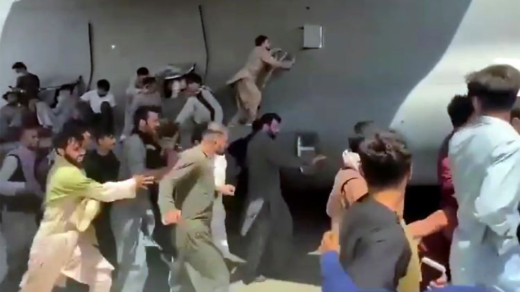 Aufnahmen zeigen Menschen, die sich an die Außenseite einer US-Militärmaschine klammern.