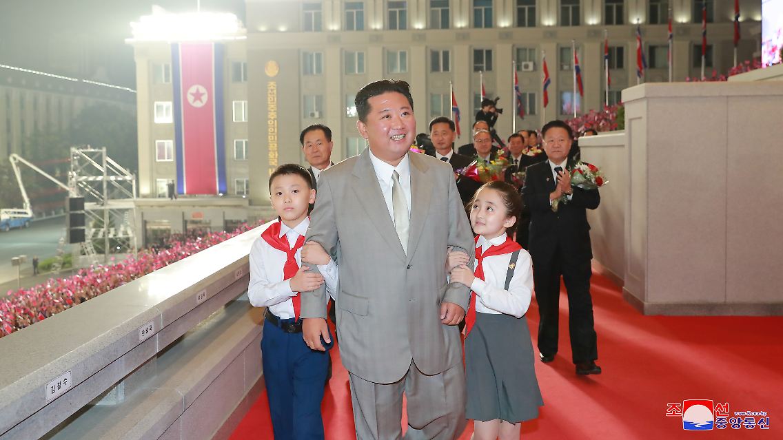 Machthaber Kim Jong Un zeigt sich im hellgrauen westlichen Anzug und einer dazu passenden Krawatte vor der jubelnden Menge, ...