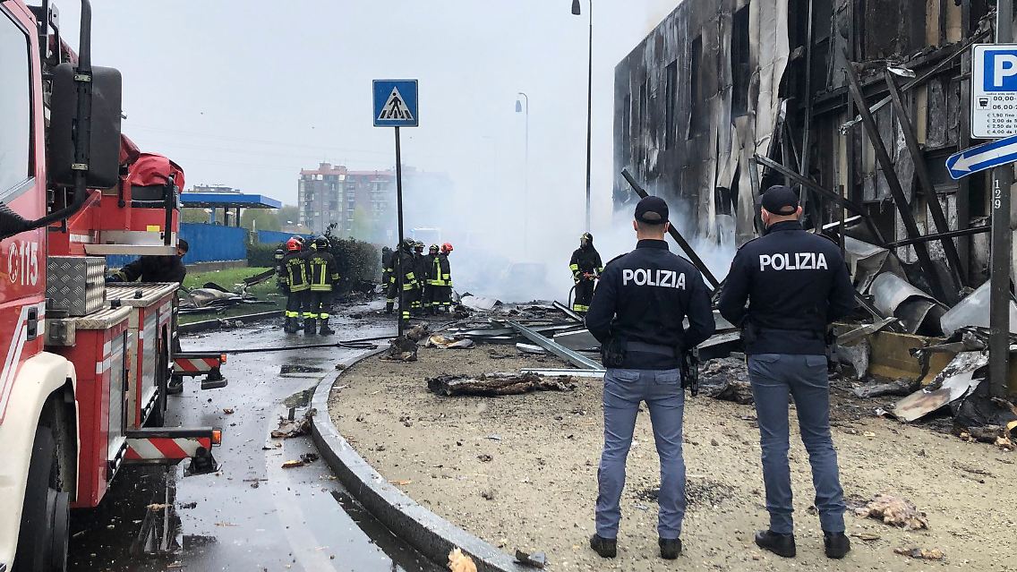 Feuerwehrleute und Polizisten stehen an der Absturzstelle eines Flugzeugs in San Donato, einem Vorort von Mailand.