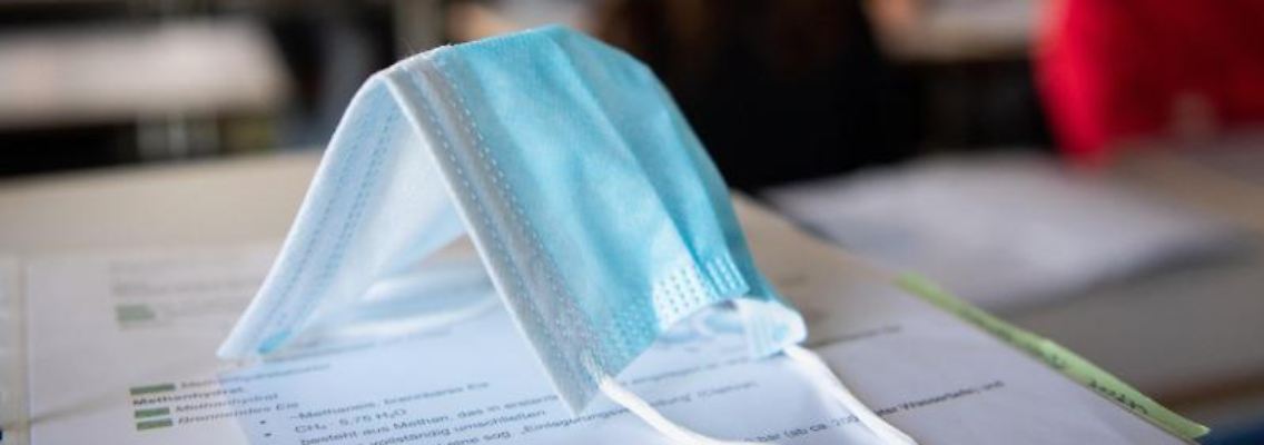 Ein Mund-Nasen-Schutz liegt im Unterricht auf Unterlagen. Foto: Matthias Balk/dpa/Symbolbild