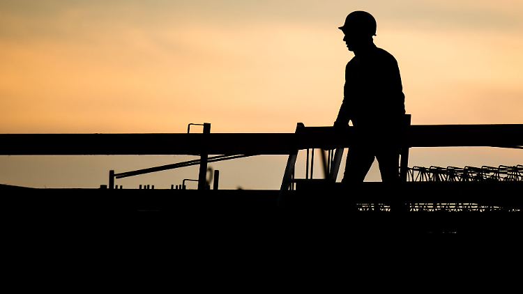 Die Silhouette eines Bauarbeiters zeichnet sich vor dem verfärbten Morgenhimmel ab.