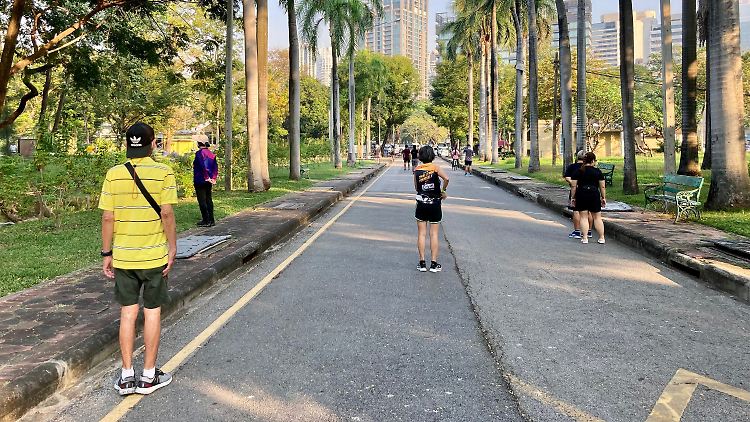 Jogger und Spaziergänger stehen in Bangkok still, während morgens im Lumphini Park die Nationalhymne erklingt.