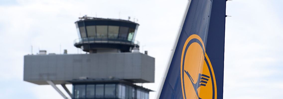 Das Logo am Leitwerk einer Lufthansa-Maschine ist vor der Kulisse eines Towers zu sehen.