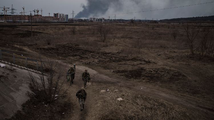 Soldaten gehen einen Weg entlang, während Rauch in Irpin nordwestlich von Kiew aufsteigt.
