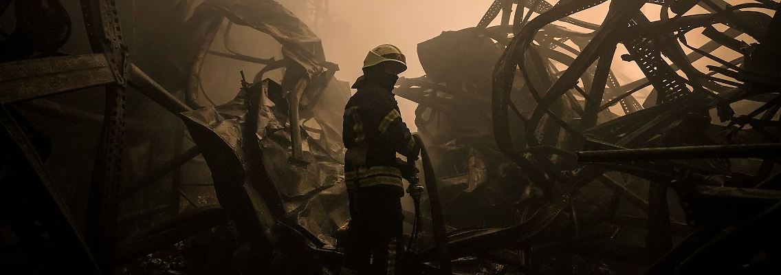 Ein ukrainischer Feuerwehrmann zieht einen Schlauch durch ein großes Lebensmittellager am Stadtrand von Kiew, das durch einen Luftangriff zerstört wurde.