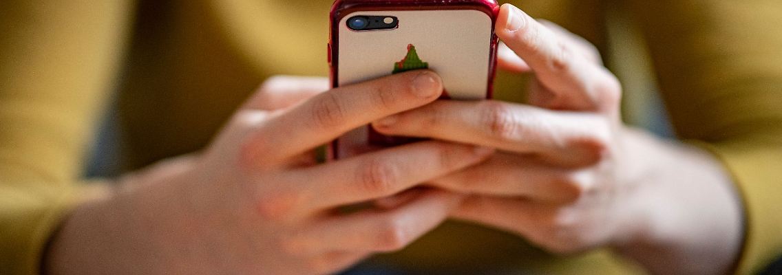 Eine junge Frau hält ein Smartphone in der Hand.
