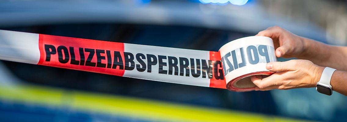 Eine Polizistin rollt ein Absperrband aus.