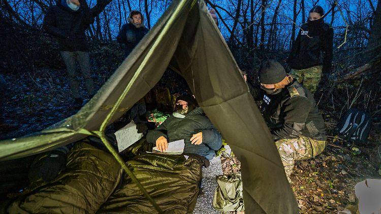 Eine polnische Grenzschutzbeamtin kontrolliert im November 2021 zwei syrische Geflüchtete in einem Wald in Polen.