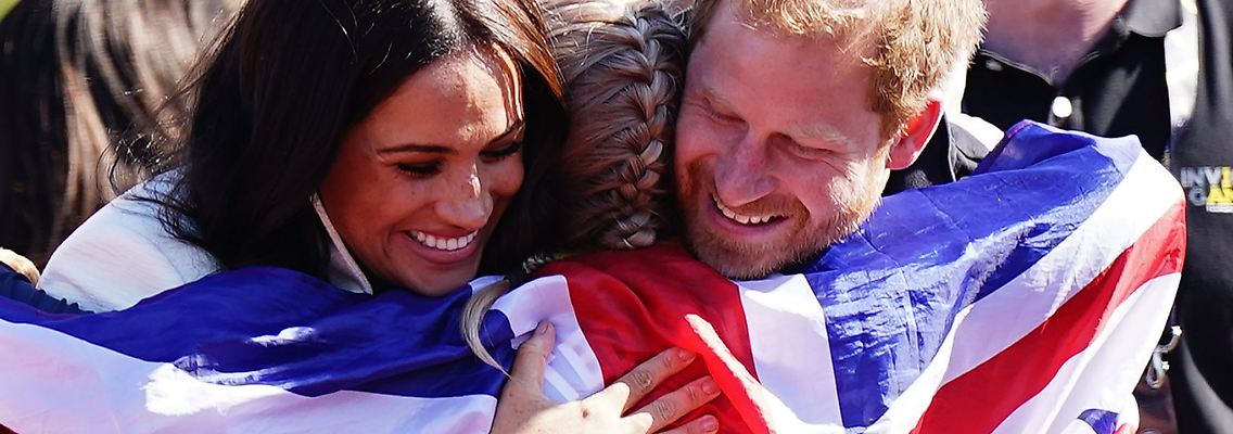 Prinz Harry (r) und Meghan (l) umarmen die britische Teilnehmerin Lisa Johnston.