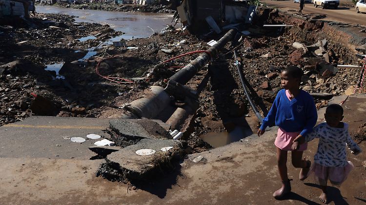 Kinder gehen auf einer durch Überschwemmungen beschädigten Straße in Durban. 