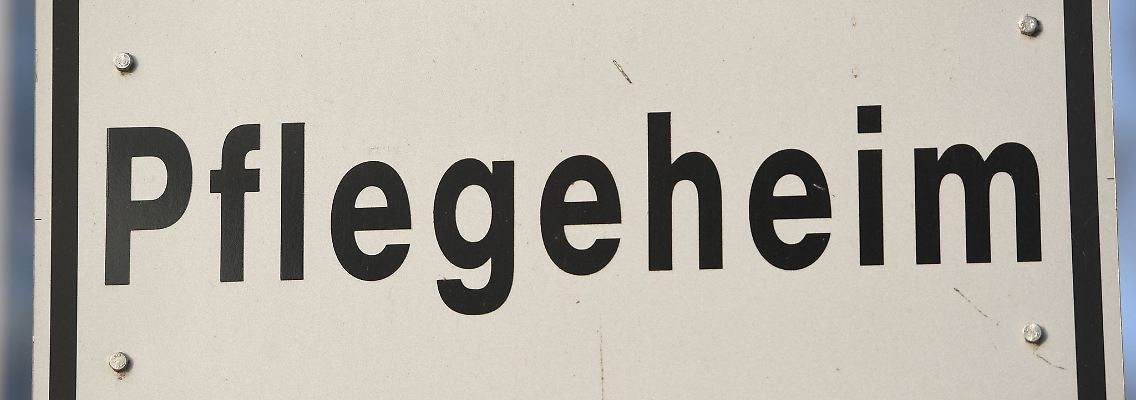 Ein Schild mit der Aufschrift "Pflegeheim" steht an einer Straße.