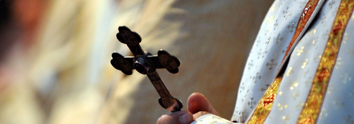 Ein katholischer Bischof hält während einer Messe ein Kreuz in den Händen.