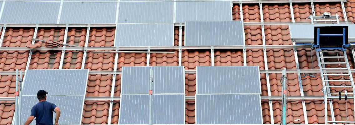 Ein Arbeiter installiert auf einem Dach eine Solaranlage.