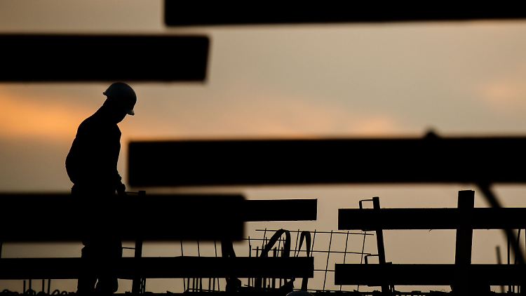 Die Silhouette eines Arbeiters zeichnet sich auf einer Baustelle vor dem verfärbten Morgenhimmel ab.