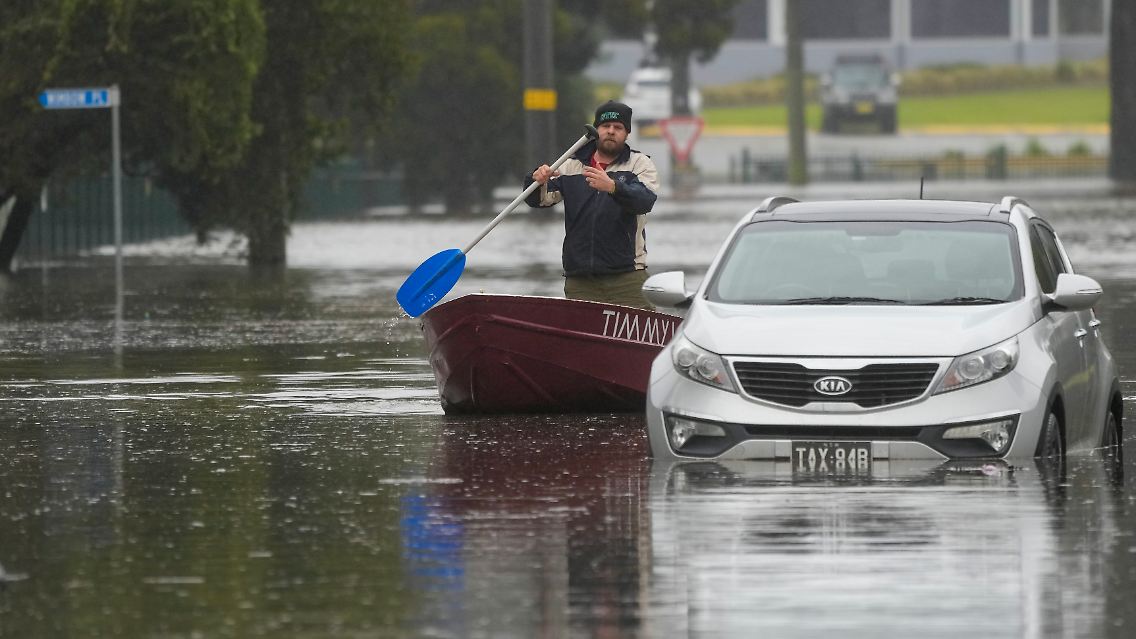 Ein Mann paddelt mit seinem Boot auf einer überfluteten Straße am Stadtrand von Sydney.