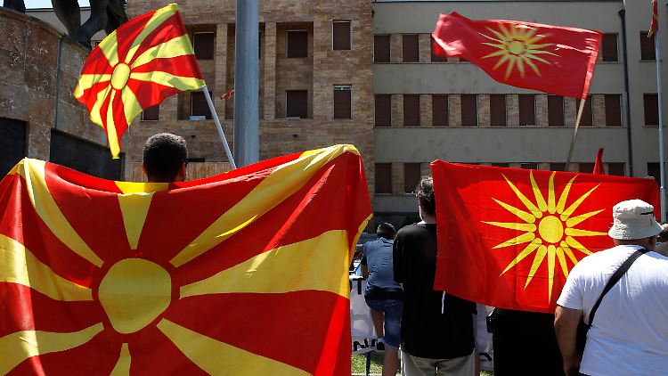 Während im Parlament abgestimmt wird, protestieren draußen Menschen - und schwenken dabei auch die alte Flagge des Landes (r.), die Teil des Streits mit Griechenland war.