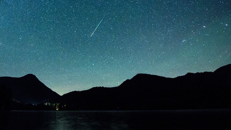 Eine Sternschnuppe leuchtet vor der Milchstraße am Himmel über dem Walchensee.