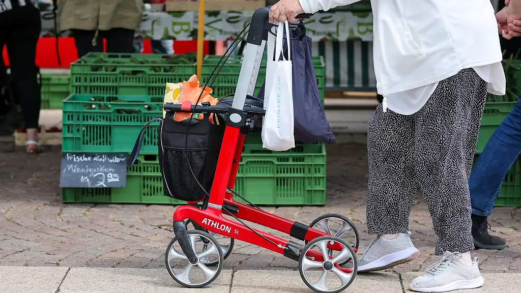 Eine-Seniorin-geht-mit-ihrem-Rollator-ueber-den-Wochenmarkt-in-der-Innenstadt